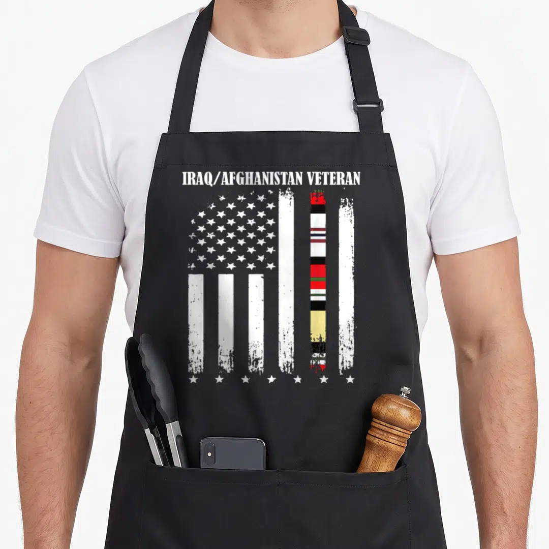 Proud afghanistan apron - Distressed USA flag with colorful ribbon stripe and Iraq Afghanistan Veteran text — shown on a black cotton canvas apron against a white background