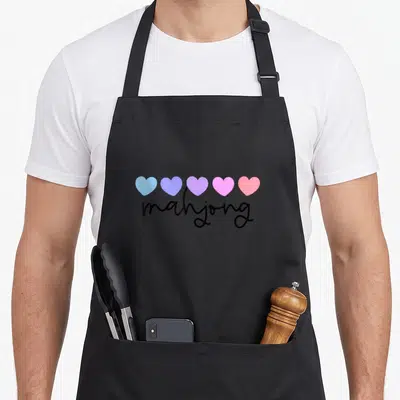 Funny mahjong apron - Five blue purple pink and red hearts above black mahjong script text — shown on a black cotton canvas apron against a white background
