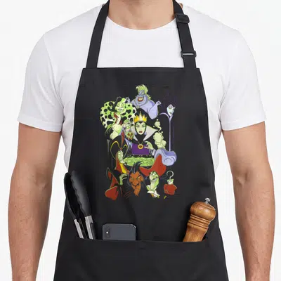 Cauldron novelty apron - Evil Queen holding green apple over cauldron surrounded by other villains in purple and green — shown on a black cotton canvas apron against a white background