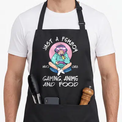 Femboy anime apron - Cartoon person sitting cross-legged with purple hair holding a controller and eating chocolate — shown on a black cotton canvas apron against a white background