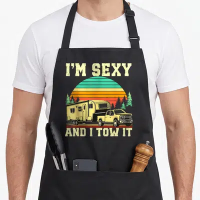 Camping truck apron - Retro pickup truck towing camper under striped sun with text I'M SEXY AND I TOW IT — shown on a black cotton canvas apron against a white background