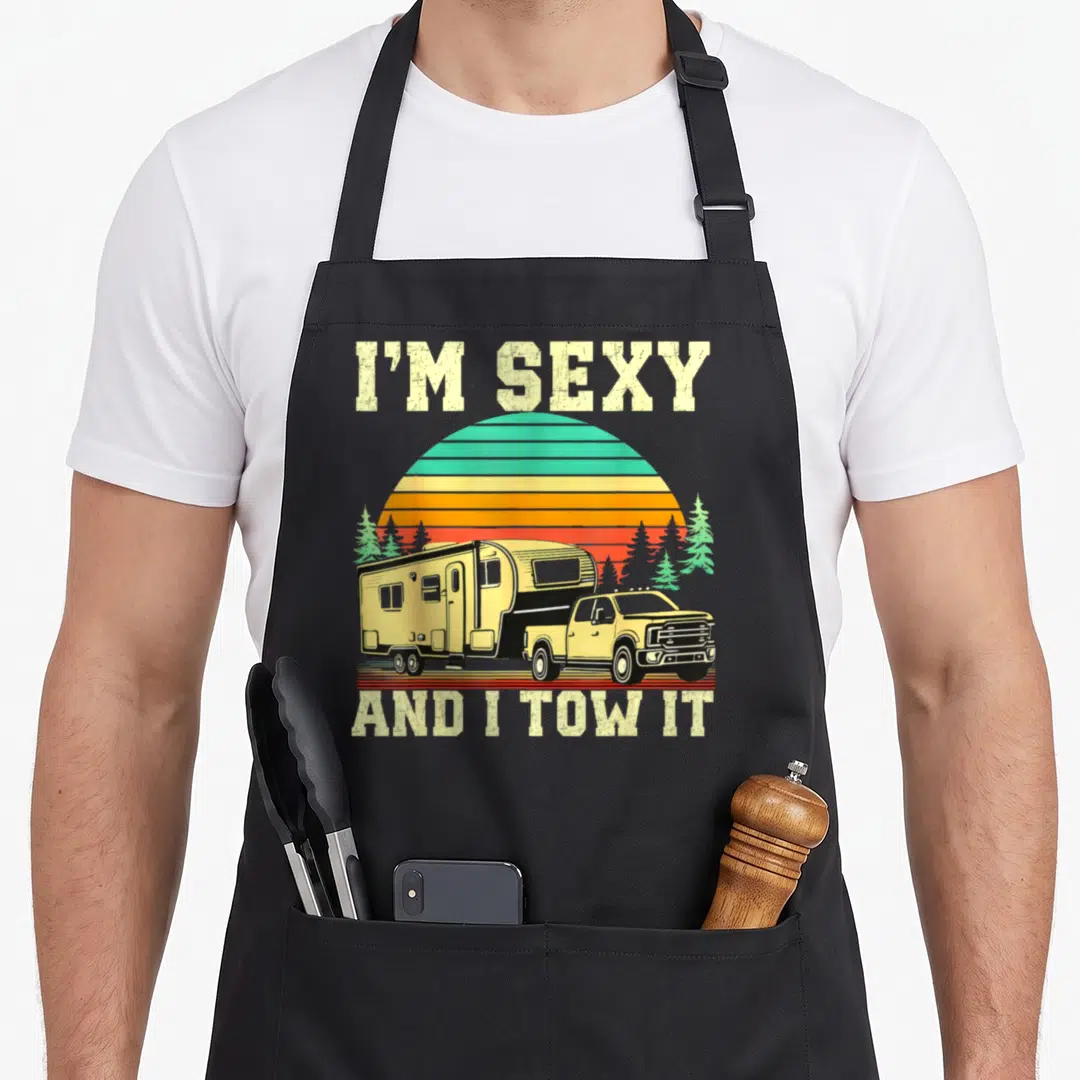 Camping truck apron - Retro pickup truck towing camper under striped sun with text I'M SEXY AND I TOW IT — shown on a black cotton canvas apron against a white background