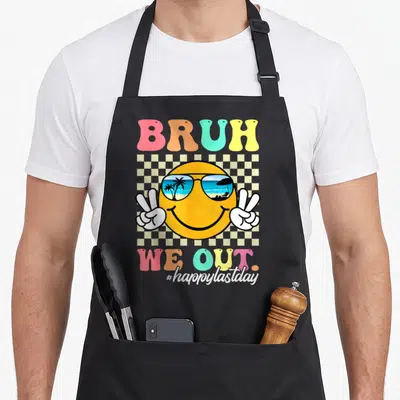 School summer teacher apron - Retro smiley face with sunglasses, peace hands, and Bruh We Out text on checkerboard — shown on a black cotton canvas apron against a white background
