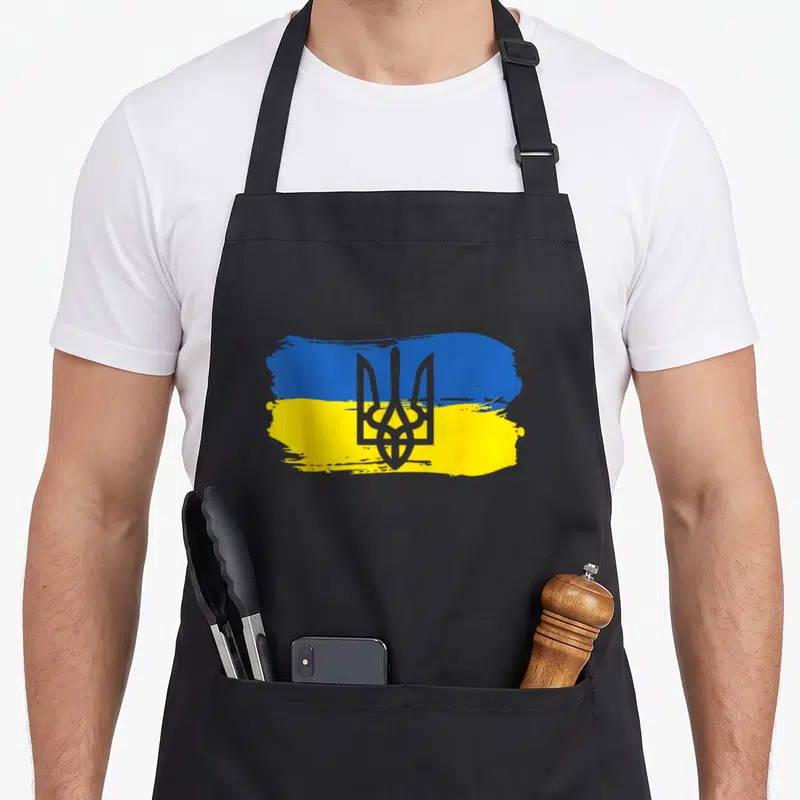 Ukraine ukrainian aprons - Grey trident on blue and yellow brush-stroke flag, cartoon style — shown on a black cotton canvas apron against a white background
