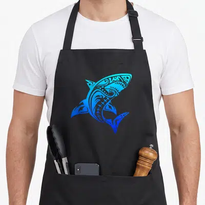 Throwback shark apron - Stylized blue and cyan shark with tribal line art patterns centered on grey background — shown on a black cotton canvas apron against a white background