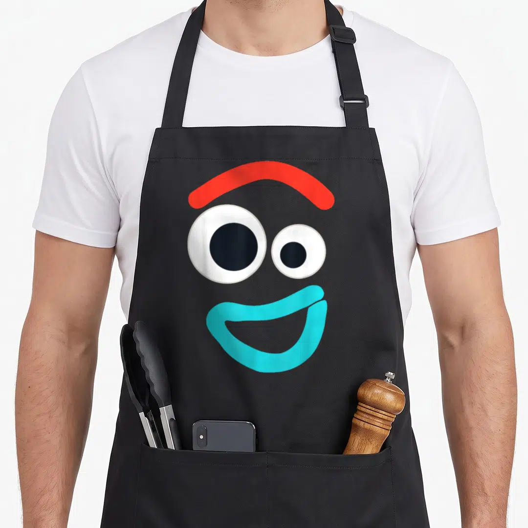 Forky camping apron - Cartoon face with red eyebrow, two white eyes, and light blue smile — shown on a black cotton canvas apron against a white background