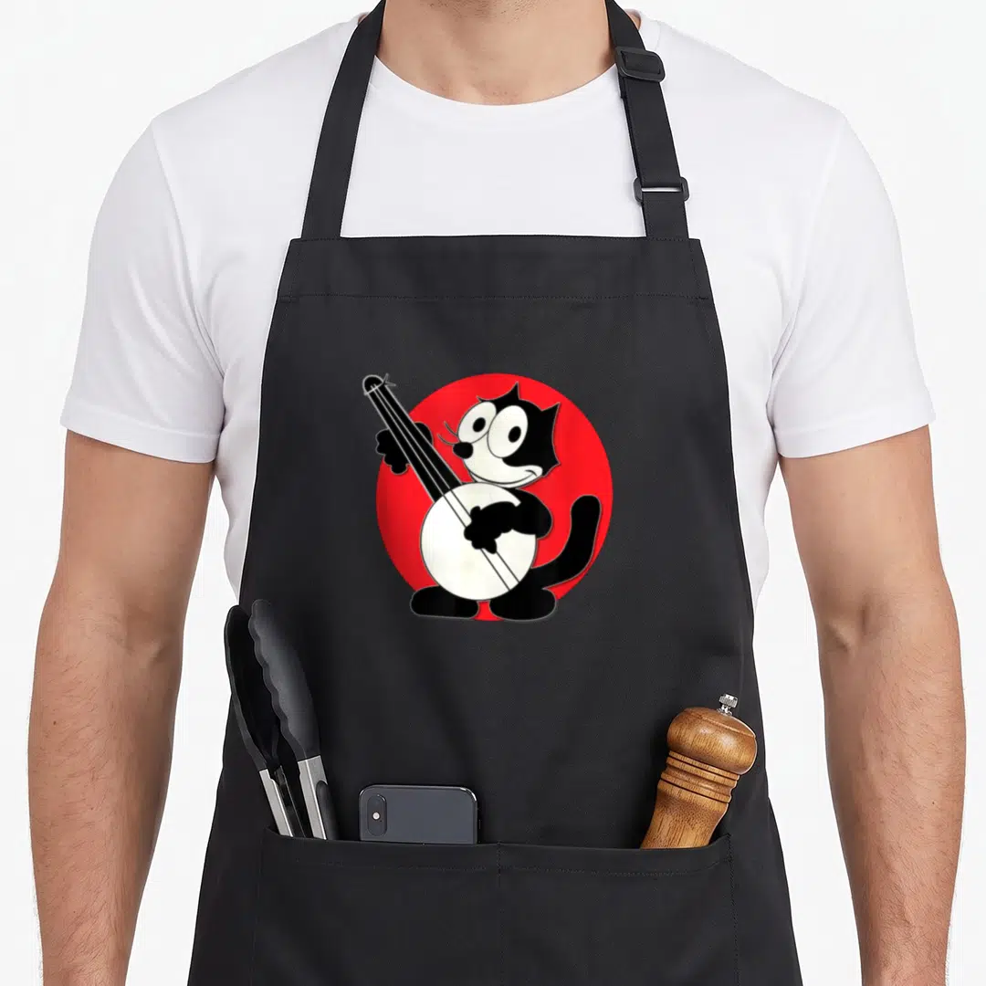 Play cartoon apron - Black and white cartoon cat playing banjo on red circle — shown on a black cotton canvas apron against a white background