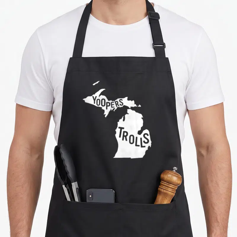 Yooper michigan boy apron - White Michigan map silhouette with YOOPERS text in Upper Peninsula and TROLLS in Lower — shown on a black cotton canvas apron against a white background