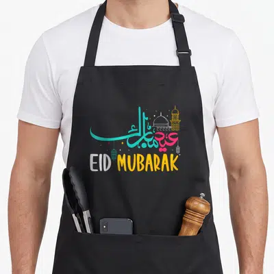 Ramadan eid al fitr apron - EID MUBARAK calligraphy with teal pink yellow mosque lanterns and stars — shown on a black cotton canvas apron against a white background