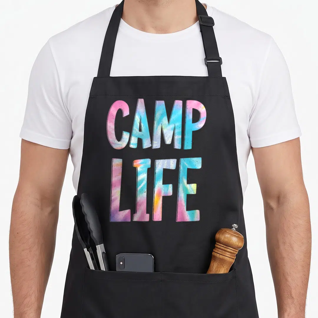 Tie camp chef apron - CAMP LIFE tie-dye text in pink blue yellow purple stacked block letters — shown on a black cotton canvas apron against a white background