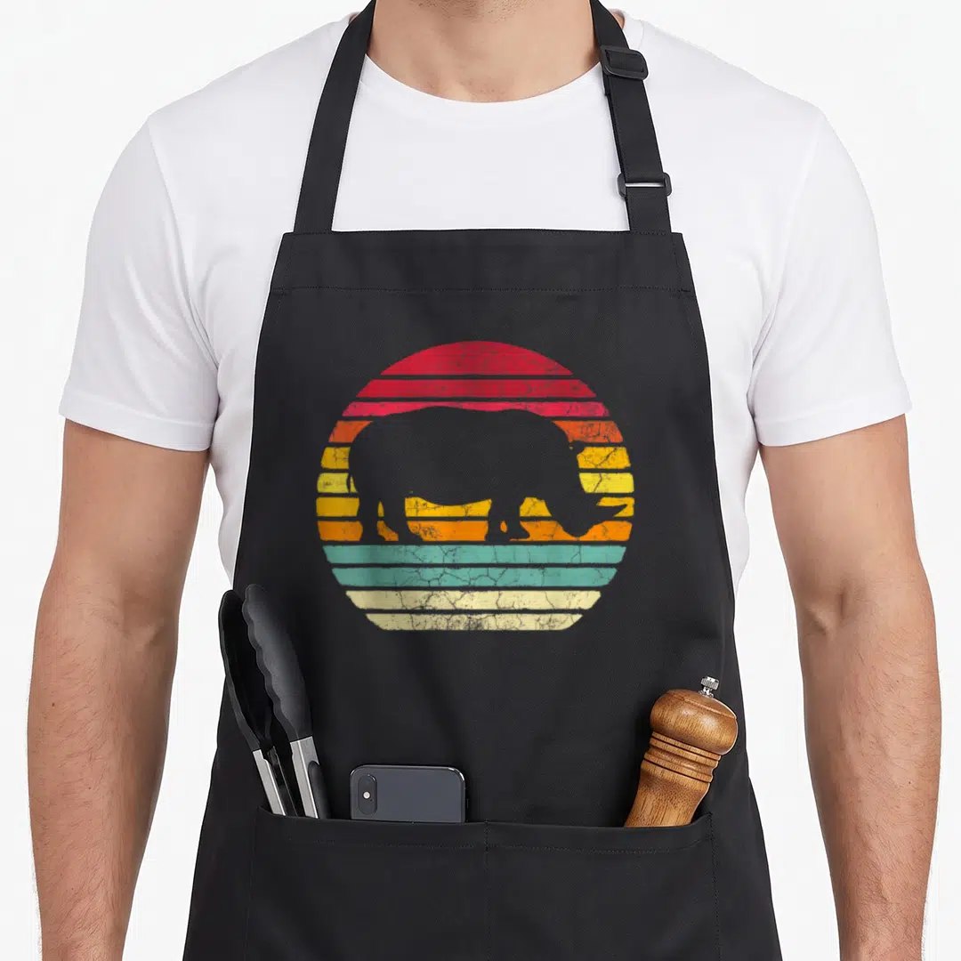 Rhinocero rhino apron - Grey rhino silhouette over circular sunset with red orange yellow blue and beige stripes — shown on a black cotton canvas apron against a white background
