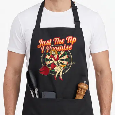 Tip pinup apron - Cartoon woman sitting on dartboard holding large dart under arched text Just The Tip I Promise — shown on a black cotton canvas apron against a white background