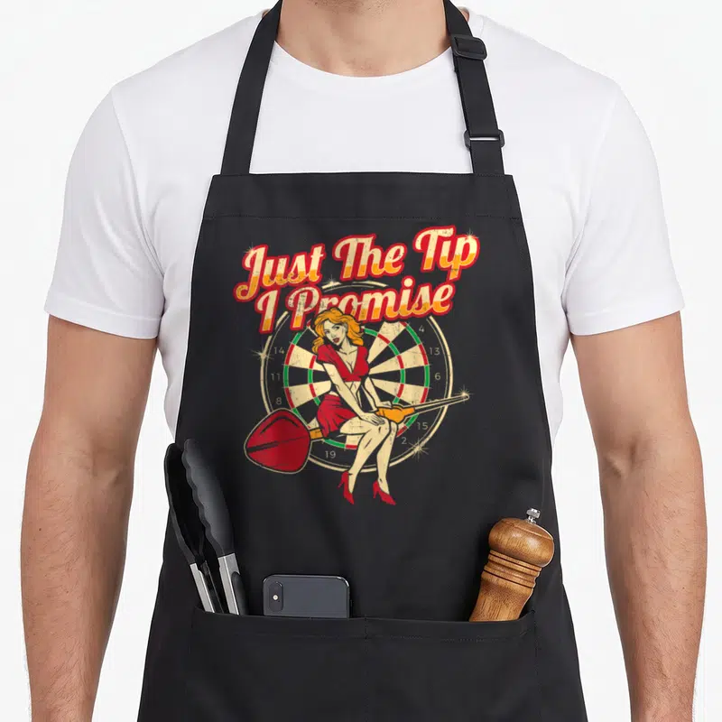 Tip pinup apron - Cartoon woman sitting on dartboard holding large dart under arched text Just The Tip I Promise — shown on a black cotton canvas apron against a white background