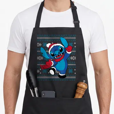 Holiday stitch apron - Blue cartoon character in red hat and scarf surrounded by snowflakes and dots — shown on a black cotton canvas apron against a white background