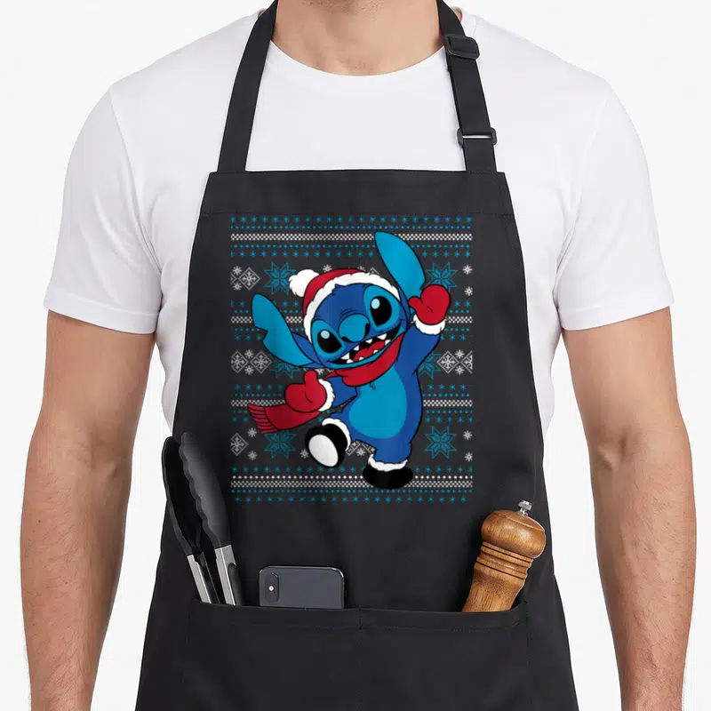 Holiday stitch apron - Blue cartoon character in red hat and scarf surrounded by snowflakes and dots — shown on a black cotton canvas apron against a white background