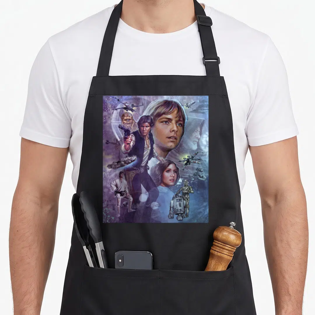 Celebration graphic novel apron - Realistic Star Wars character montage with Luke Skywalker and spacecraft in blue — shown on a black cotton canvas apron against a white background