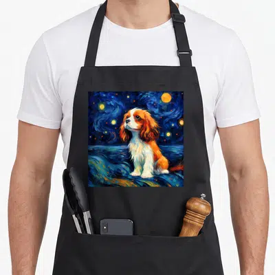 Surreal king apron - Cavalier King Charles Spaniel dog sitting on blue swirling clouds under a starry night sky — shown on a black cotton canvas apron against a white background