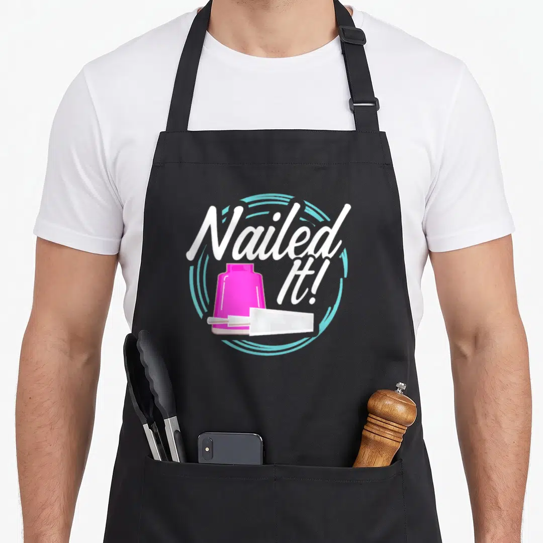 Nailed manicurist apron - Pink nail polish bottle and brush with Nailed It! text in light blue circle — shown on a black cotton canvas apron against a white background