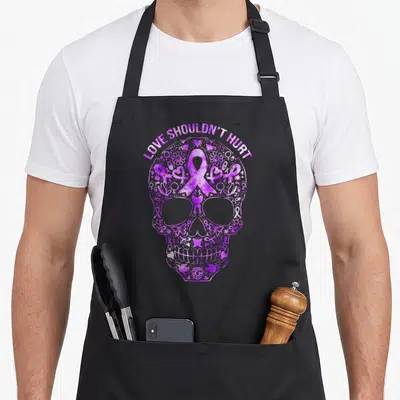 Sugar domestic aprons - Purple skull made of ribbons and hearts with LOVE SHOULDN'T HURT text — shown on a black cotton canvas apron against a white background