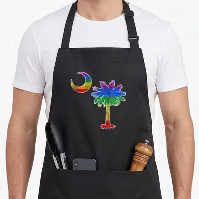 Carolina gay pride apron - Rainbow striped crescent moon left of palm tree in purple blue green yellow orange red — shown on a black cotton canvas apron against a white background