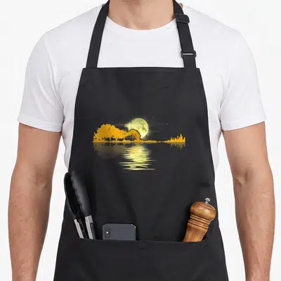 Guitar musician apron - Yellow moon and grey skyline silhouette reflected in water on black fabric — shown on a black cotton canvas apron against a white background