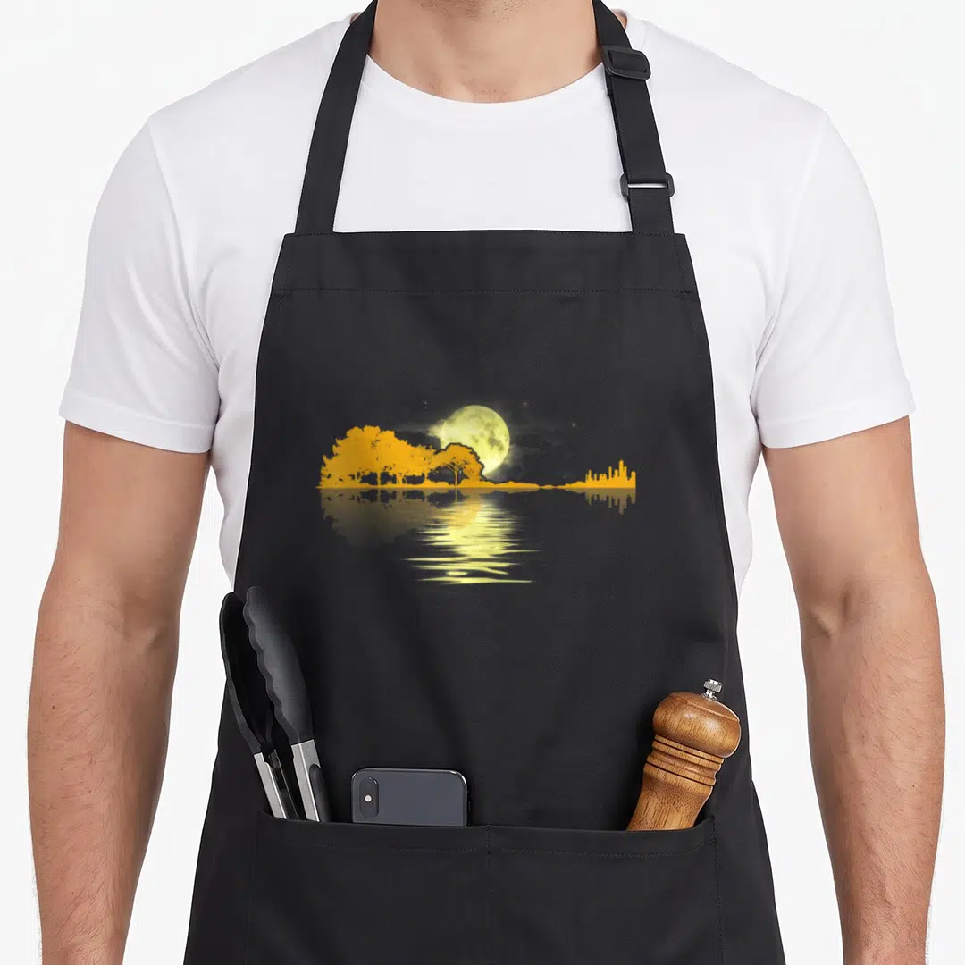 Guitar musician apron - Yellow moon and grey skyline silhouette reflected in water on black fabric — shown on a black cotton canvas apron against a white background