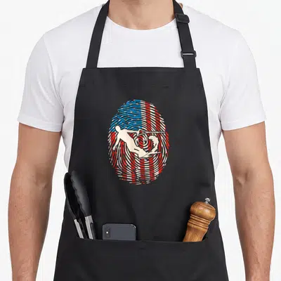 Wakeboarding american flag apron - White surfer silhouette inside oval fingerprint pattern with red white and blue flag — shown on a black cotton canvas apron against a white background
