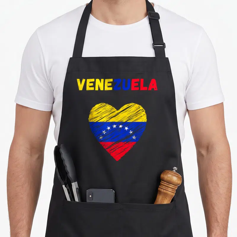Venezuela holiday apron - Heart filled with yellow blue and red flag stripes below VENEZUELA text — shown on a black cotton canvas apron against a white background