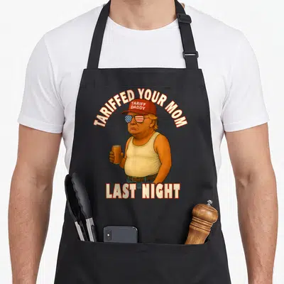 Tariffed meme apron - Cartoon man with tariff daddy hat and TARIFFED YOUR MOM LAST NIGHT text — shown on a black cotton canvas apron against a white background
