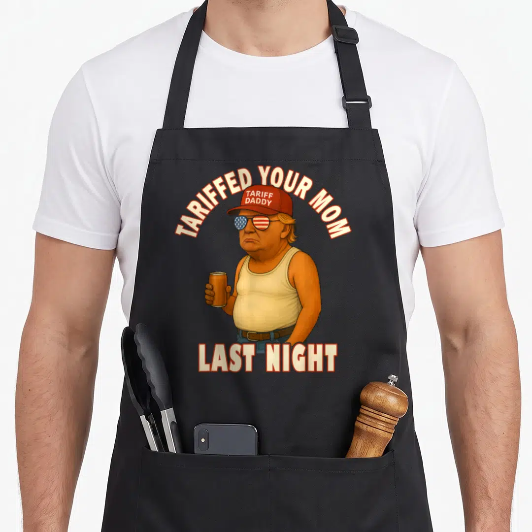 Tariffed meme apron - Cartoon man with tariff daddy hat and TARIFFED YOUR MOM LAST NIGHT text — shown on a black cotton canvas apron against a white background
