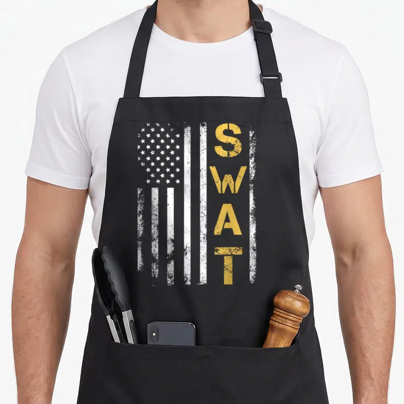 Retired swat bbq apron - Vertical white flag with gold distressed letters S W A T stacked vertically on right side — shown on a black cotton canvas apron against a white background