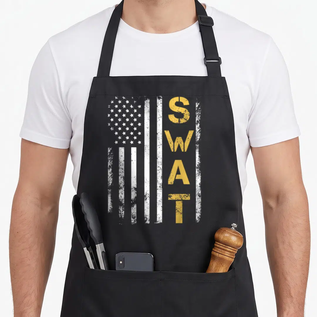 Retired swat bbq apron - Vertical white flag with gold distressed letters S W A T stacked vertically on right side — shown on a black cotton canvas apron against a white background