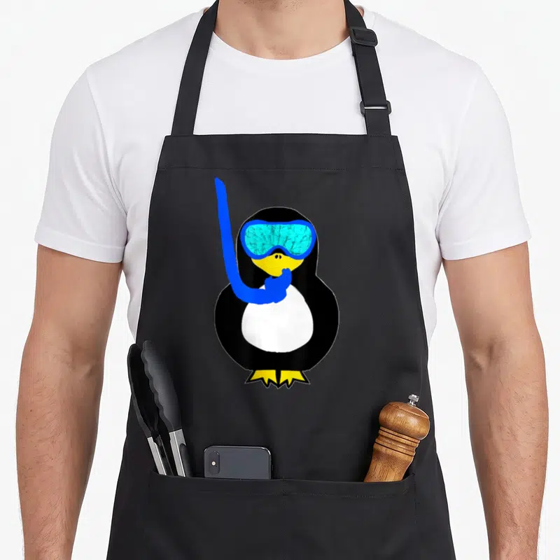 Snorkel bird apron - Cartoon penguin in black and white with blue goggles and yellow feet — shown on a black cotton canvas apron against a white background