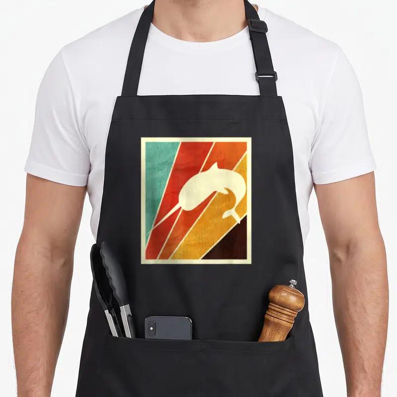 Cute narwhal apron - cream dolphin silhouette over teal red orange yellow brown diagonal stripes with cream border — shown on a black cotton canvas apron against a white background