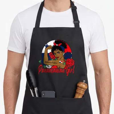 Unbreakable pride apron - Cartoon woman flexing arm with Unbreakable tattoo, Panamanian flag circle, and red and blue — shown on a black cotton canvas apron against a white background