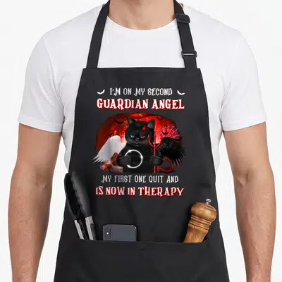 Second guardian angels and aprons - Cartoon black cat with white wing, black wing, pitchfork, and halo surrounded — shown on a black cotton canvas apron against a white background
