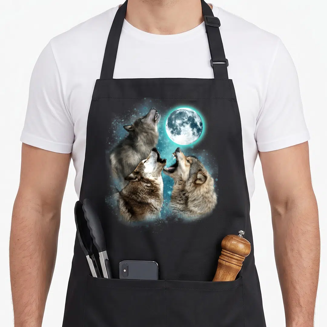 Moon wolves apron - Three realistic wolf heads howling at a full moon with blue stars — shown on a black cotton canvas apron against a white background