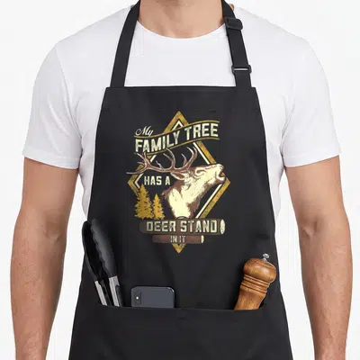 Stand tree apron - Deer head over yellow diamond with My Family Tree Has A Deer Stand In It text on logs — shown on a black cotton canvas apron against a white background
