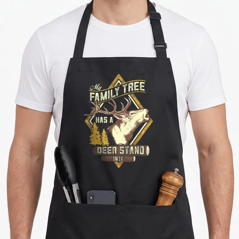 Stand tree apron - Deer head over yellow diamond with My Family Tree Has A Deer Stand In It text on logs — shown on a black cotton canvas apron against a white background