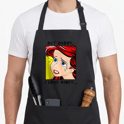 Comic daddy apron - Cartoon woman crying with red hair in yellow dotted frame and text But Daddy I Love Him — shown on a black cotton canvas apron against a white background