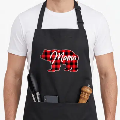 Mama red plaid apron - Cartoon bear silhouette filled with red black plaid pattern and white Mama script text — shown on a black cotton canvas apron against a white background