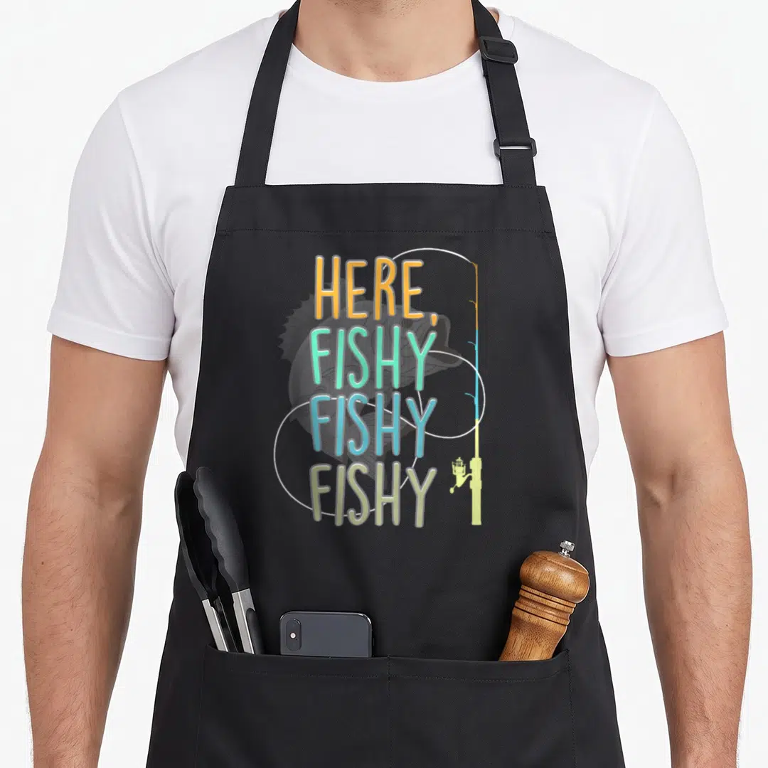 Fishy fisherman fishing aprons - Stacked HERE FISHY FISHY FISHY text in orange mint blue yellow over grey fish and rod — shown on a black cotton canvas apron against a white background