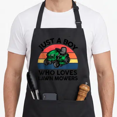 Toddler mower girl apron - Green riding mower on retro striped sun with JUST A BOY WHO LOVES LAWN MOWERS text — shown on a black cotton canvas apron against a white background