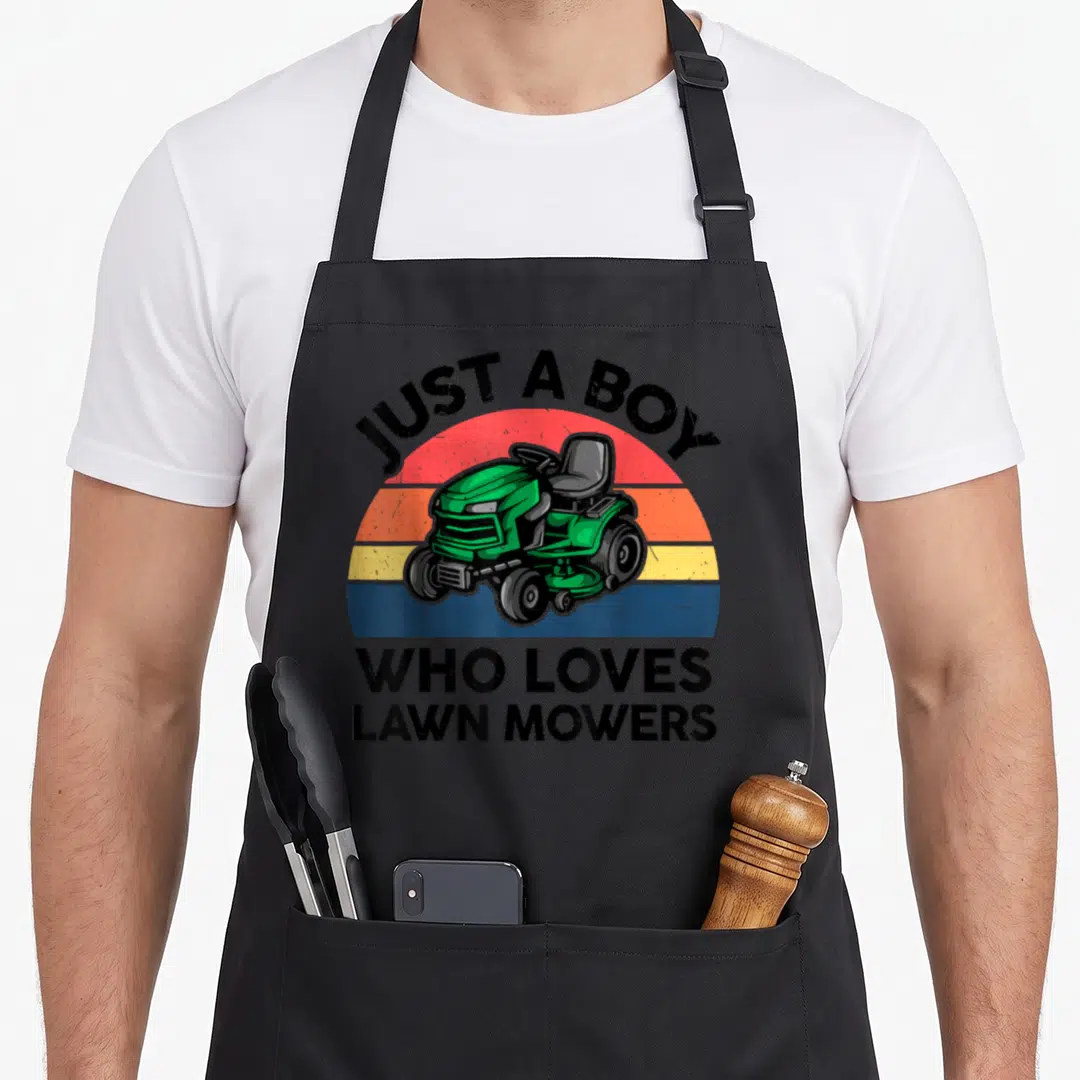 Toddler mower girl apron - Green riding mower on retro striped sun with JUST A BOY WHO LOVES LAWN MOWERS text — shown on a black cotton canvas apron against a white background
