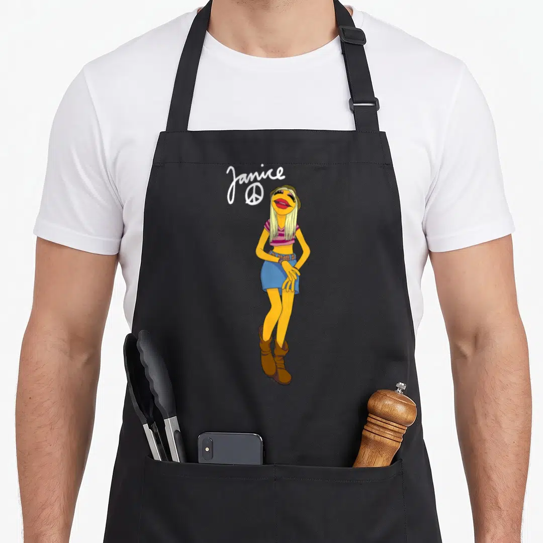 Janice big band apron - Yellow muppet wearing blue shorts and brown boots with white Janice text and peace sign — shown on a black cotton canvas apron against a white background