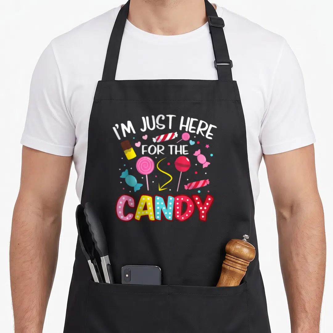 Lollipop halloween apron - Scattered lollipops and candies in white, pink, yellow, blue, red with I'M JUST HERE — shown on a black cotton canvas apron against a white background