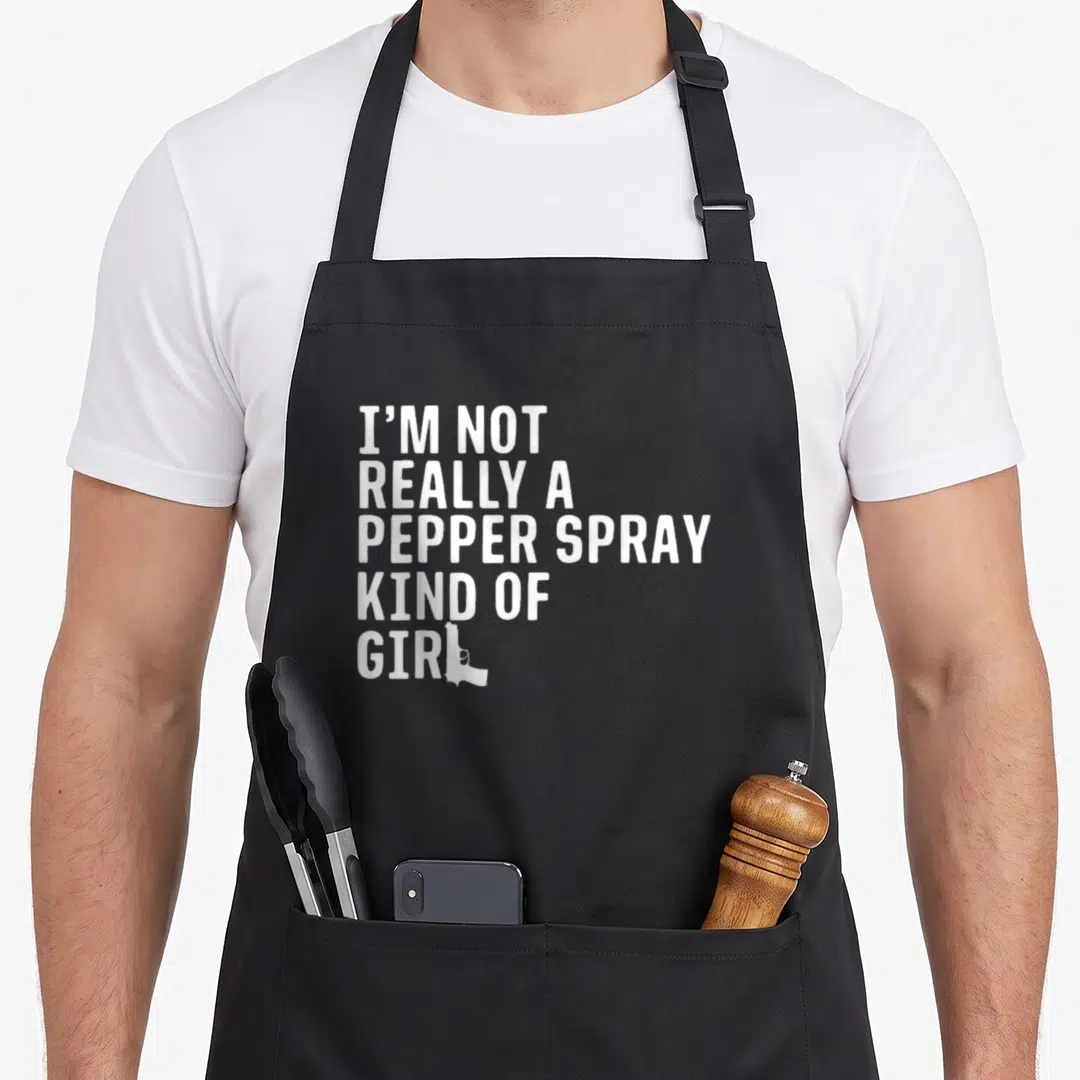 Spray pro apron - White stacked text I'm Not Really A Pepper Spray Kind Of Girl with gun silhouette replacing L — shown on a black cotton canvas apron against a white background