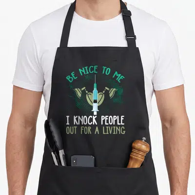 Anesthesiology anesthesiologist problems apron - Teal syringe and green lungs with text Be Nice To Me I Knock People — shown on a black cotton canvas apron against a white background