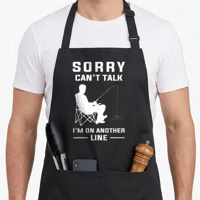 Sorry fishing aprons - White fisherman silhouette holding a rod with text Sorry Can't Talk I'm On Another Line — shown on a black cotton canvas apron against a white background