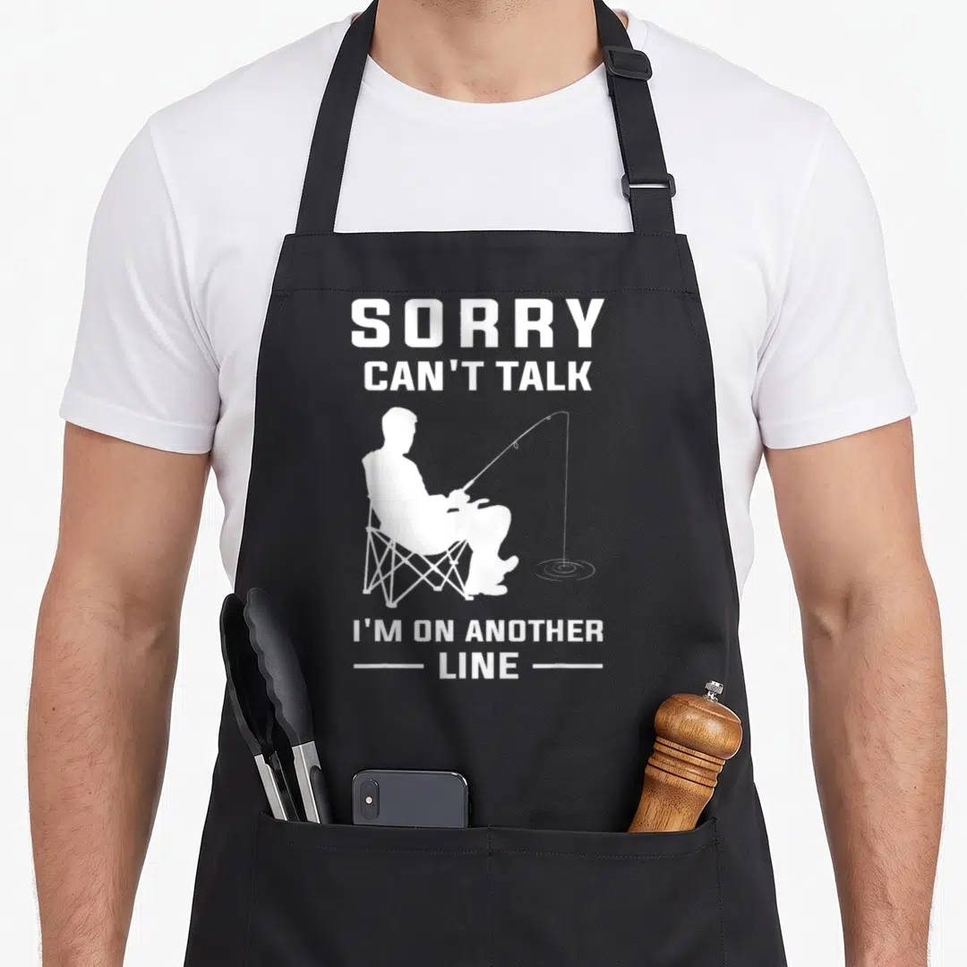 Sorry fishing aprons - White fisherman silhouette holding a rod with text Sorry Can't Talk I'm On Another Line — shown on a black cotton canvas apron against a white background